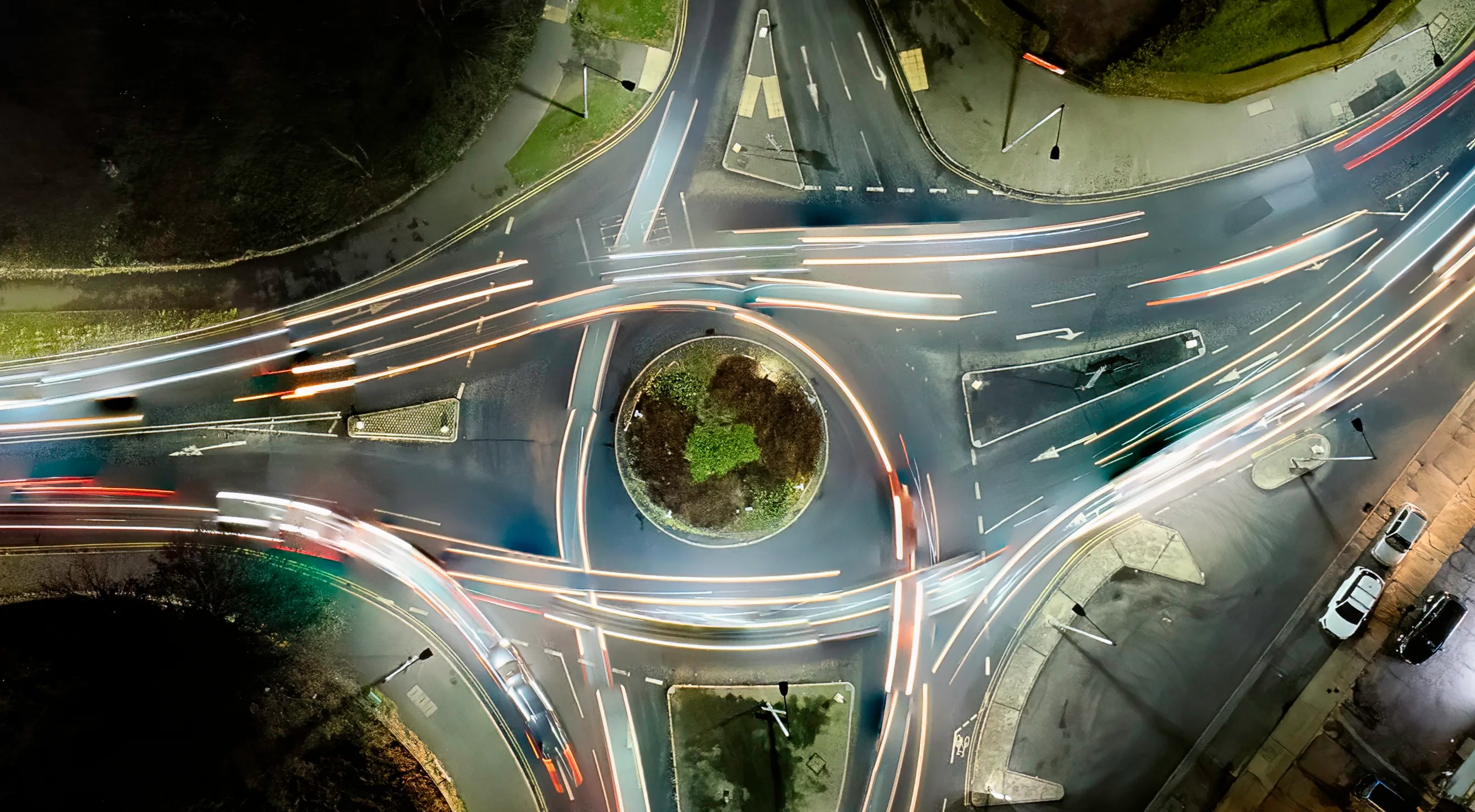 Aerial night view of a roundabout with light trails showing moving vehicles around the central island.