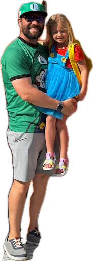 Man in costume holding daughter in colorful blue and red dress with pink sandals.