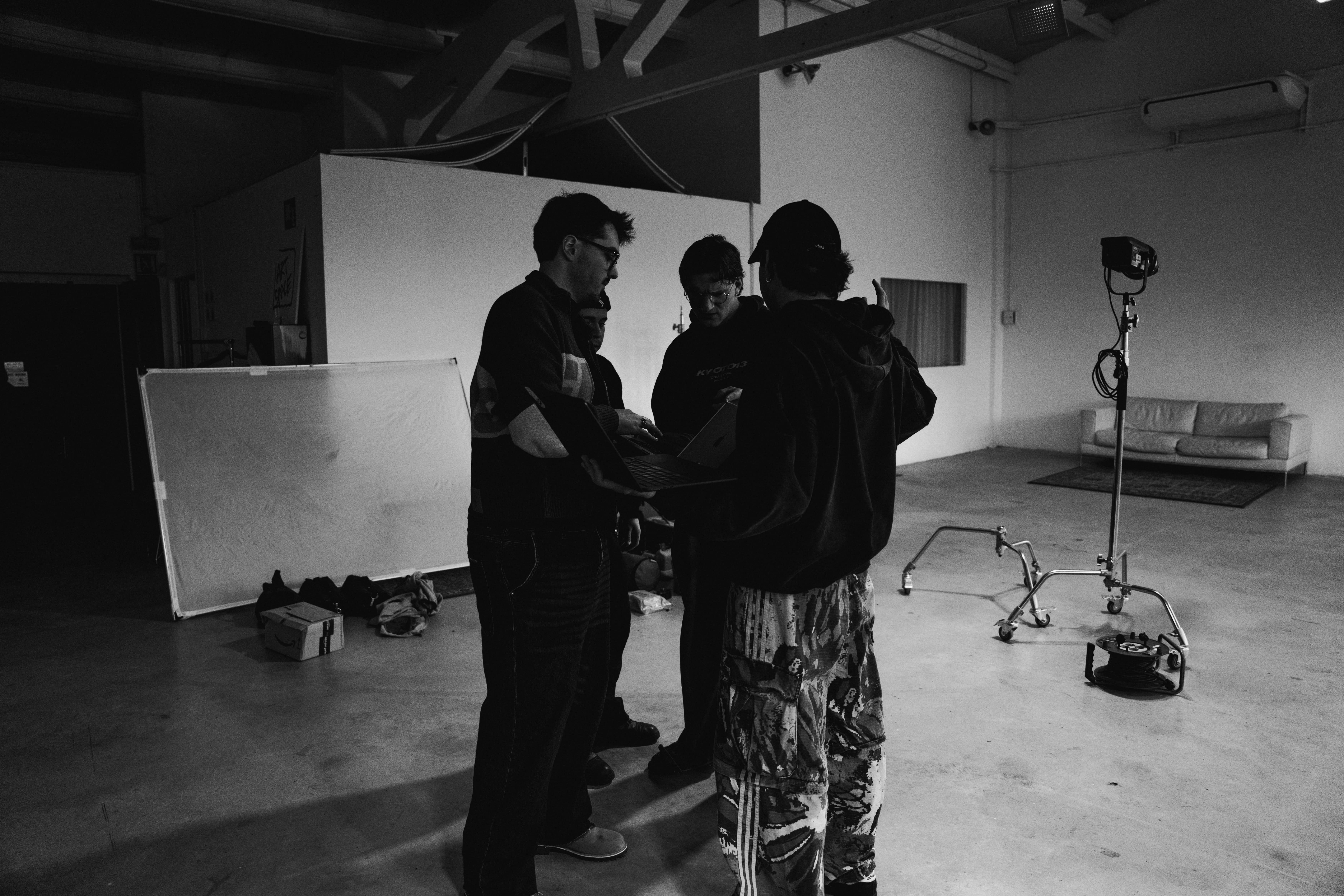 Two people sitting across from each other at a table working on laptops with a large green plant and window in the background.