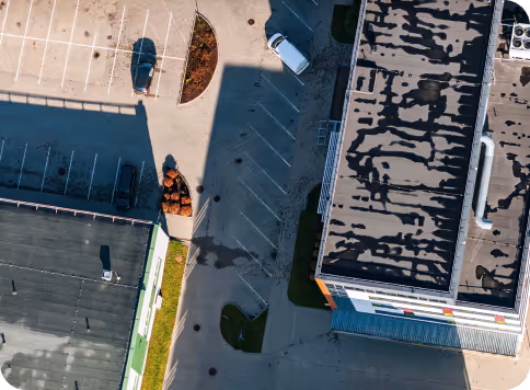 Aerial view of two buildings with parking lots, a few parked cars, and shadows cast on the pavement.