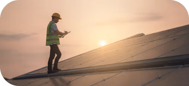 Engineer in safety vest and helmet inspecting solar panels on a rooftop at sunset.