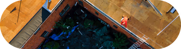 A man in red shirt working on a flat, orange-brown rooftop with scattered tools and a ladder.