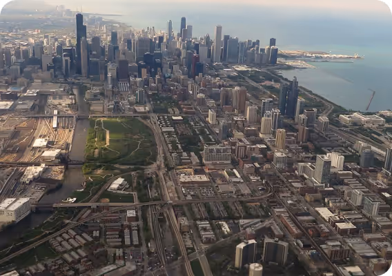 Aerial view of a large urban cityscape with skyscrapers near a waterfront and a network of roads and bridges.