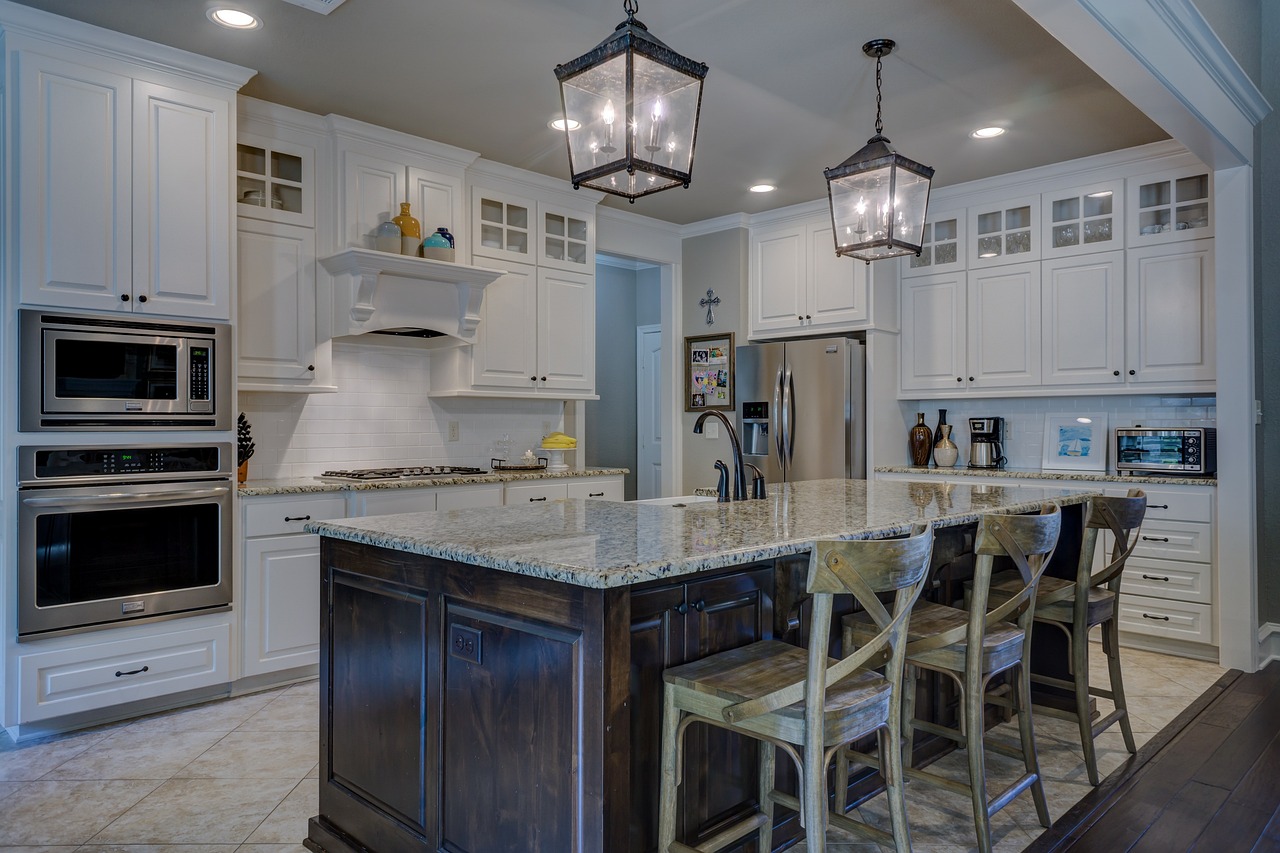 Modern kitchen with white cabinetry, stainless steel appliances, granite island countertop with wooden bar stools and hanging lantern-style lights.