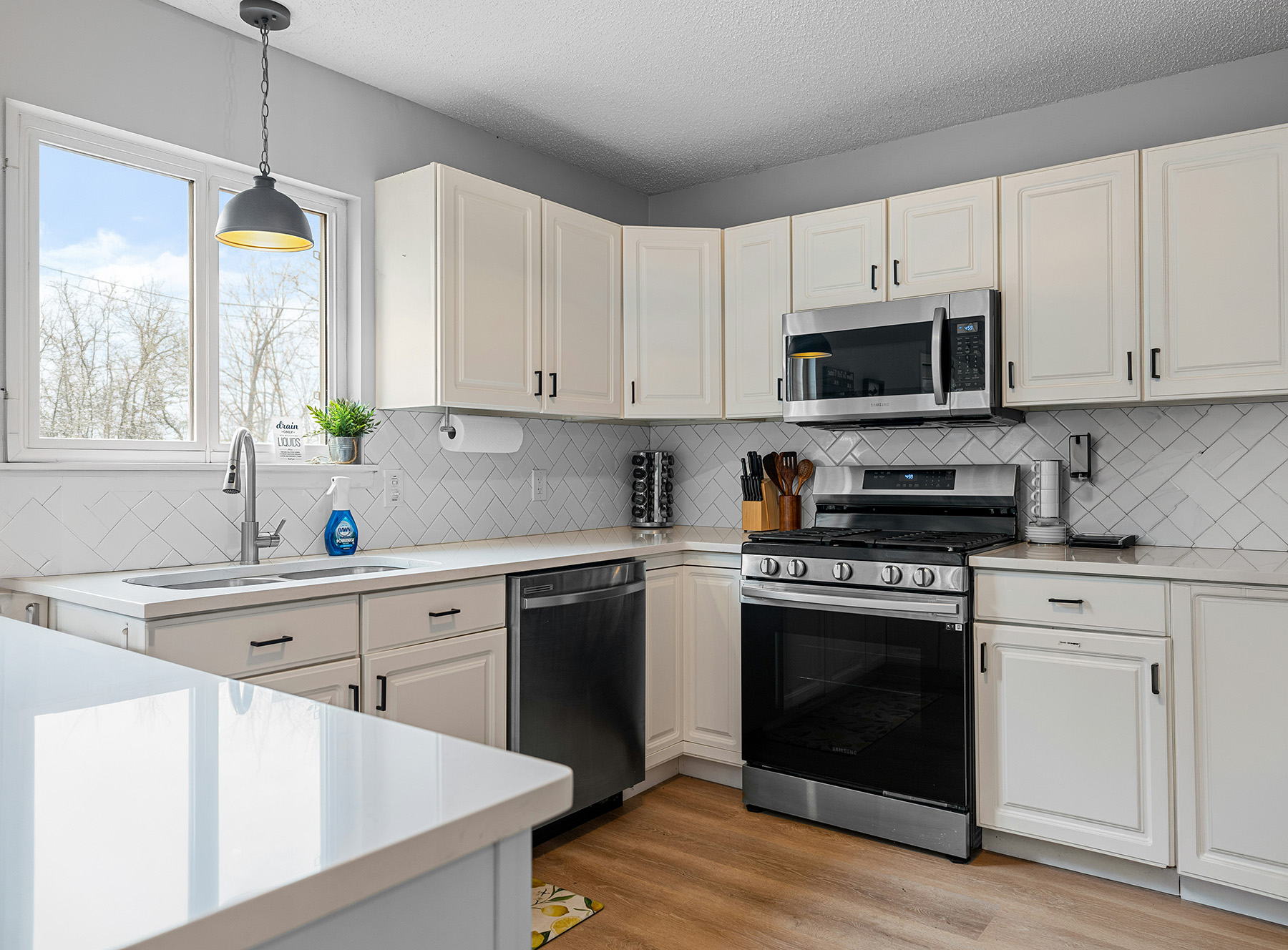Modern kitchen corner with white cabinets, stainless steel stove and microwave, dishwasher, and a window above the sink.