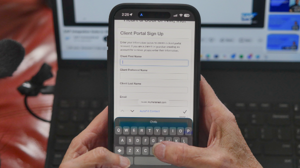 Person using a smartphone to fill out a client portal sign-up form with fields for first name, preferred name, last name, and email.