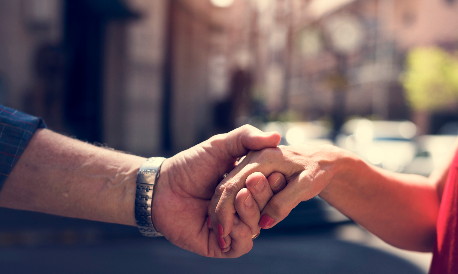 Close-up of an elderly person holding hands with another person in a warm outdoor setting.