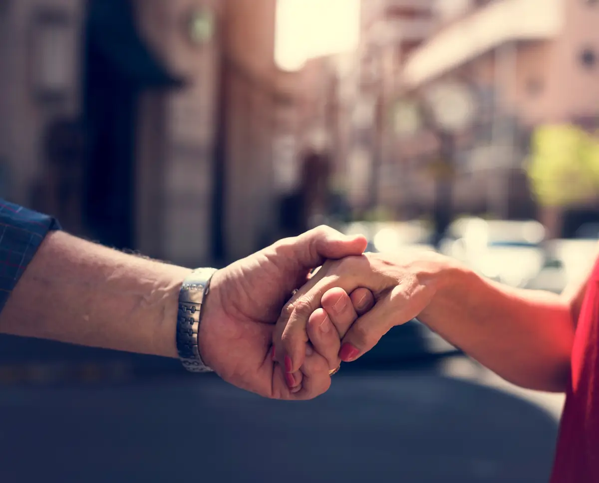 Close-up of an elderly person holding hands with another person in a warm outdoor setting.