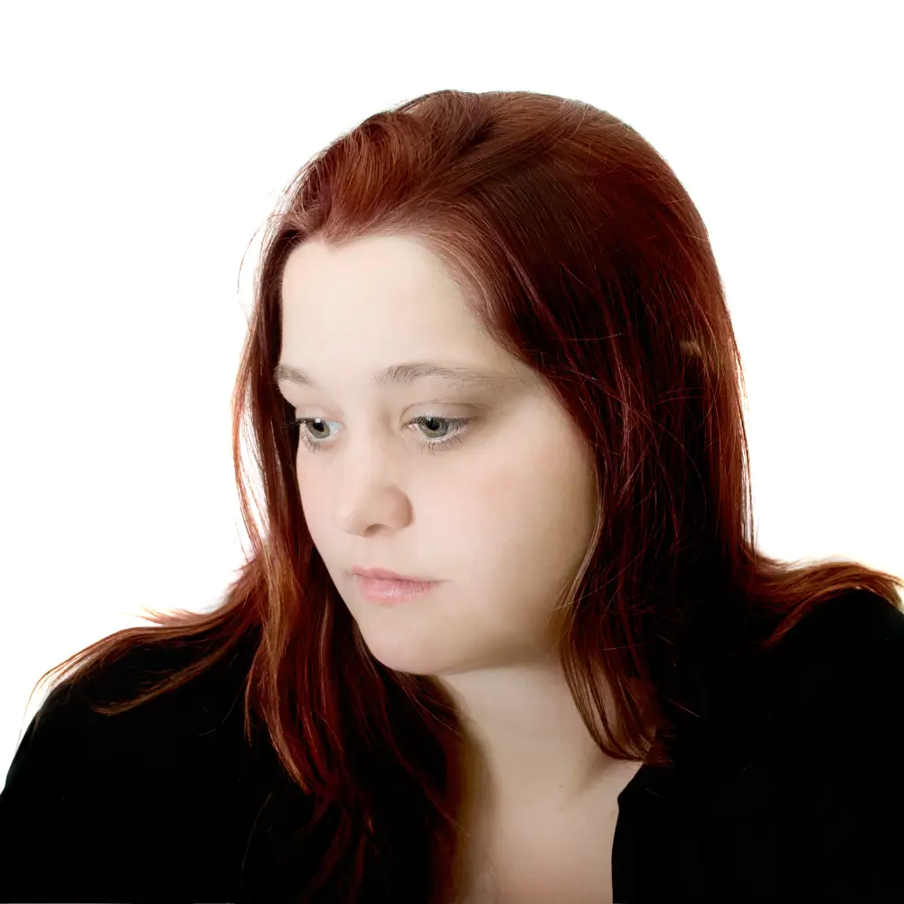 A young woman with red hair looking downward with a somber expression.