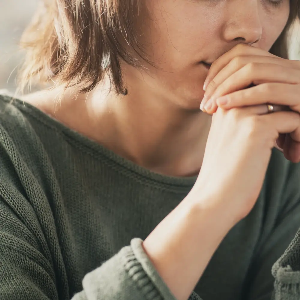 A woman holding her clasped hands to her mouth in a moment of worry or quiet distress.