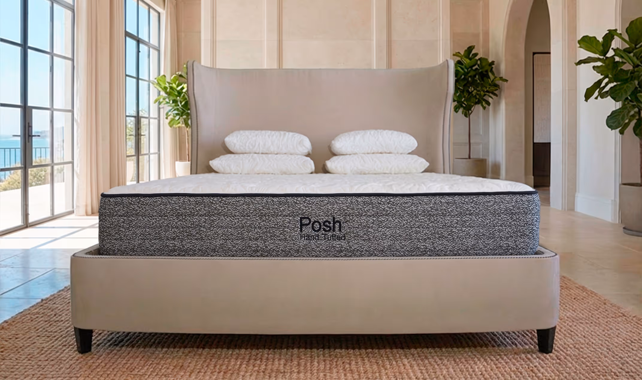 Modern bedroom with beige upholstered bed, neatly stacked white pillows, and a gray mattress labeled 'Posh Hand Tufted' in front of tall windows.