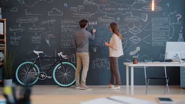 Man and woman coworkers are writing on chalk board discussing business strategy in open space office. Interior, coworking space and marketing concept.