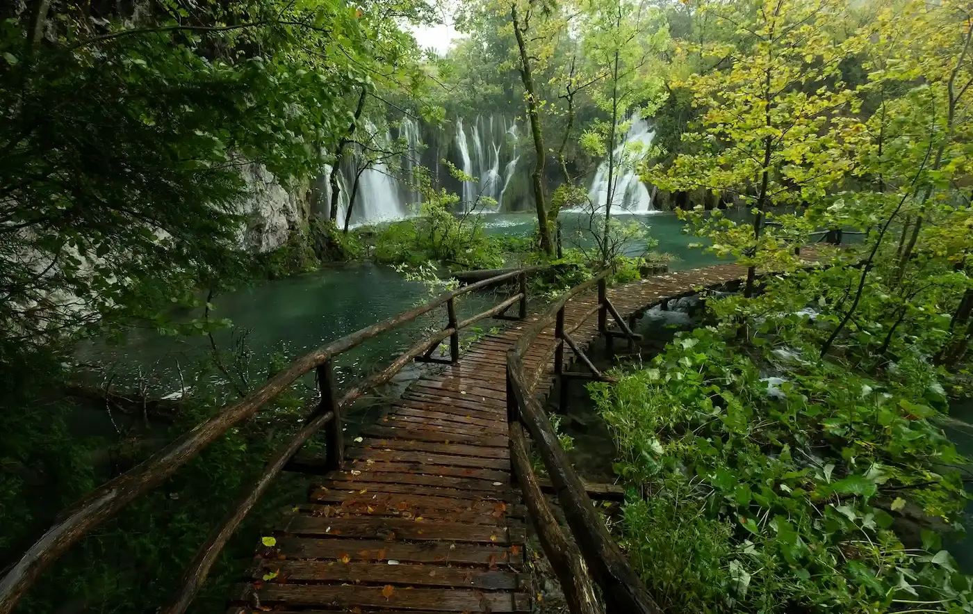 La misma pasarela de Plitvice con el bosque en verdes intensos y el agua turquesa