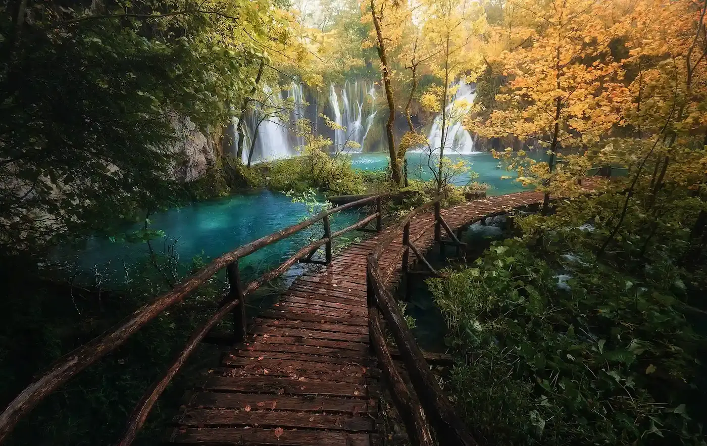 Pasarela de madera entre cascadas en Plitvice, con el bosque en naranjas y amarillos de otoño