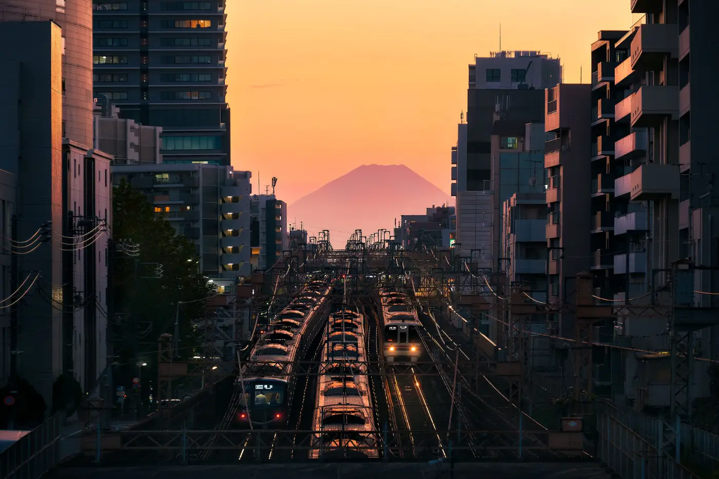 El monte Fuji al fondo de una calle de Tokio al amanecer, con las vías del tren en sombra profunda