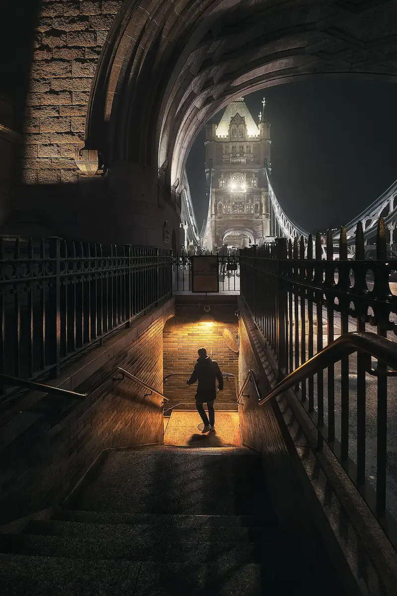 La misma escalera bajo el Tower Bridge con el azul del arco atenuado y solo la luz cálida de la escalera