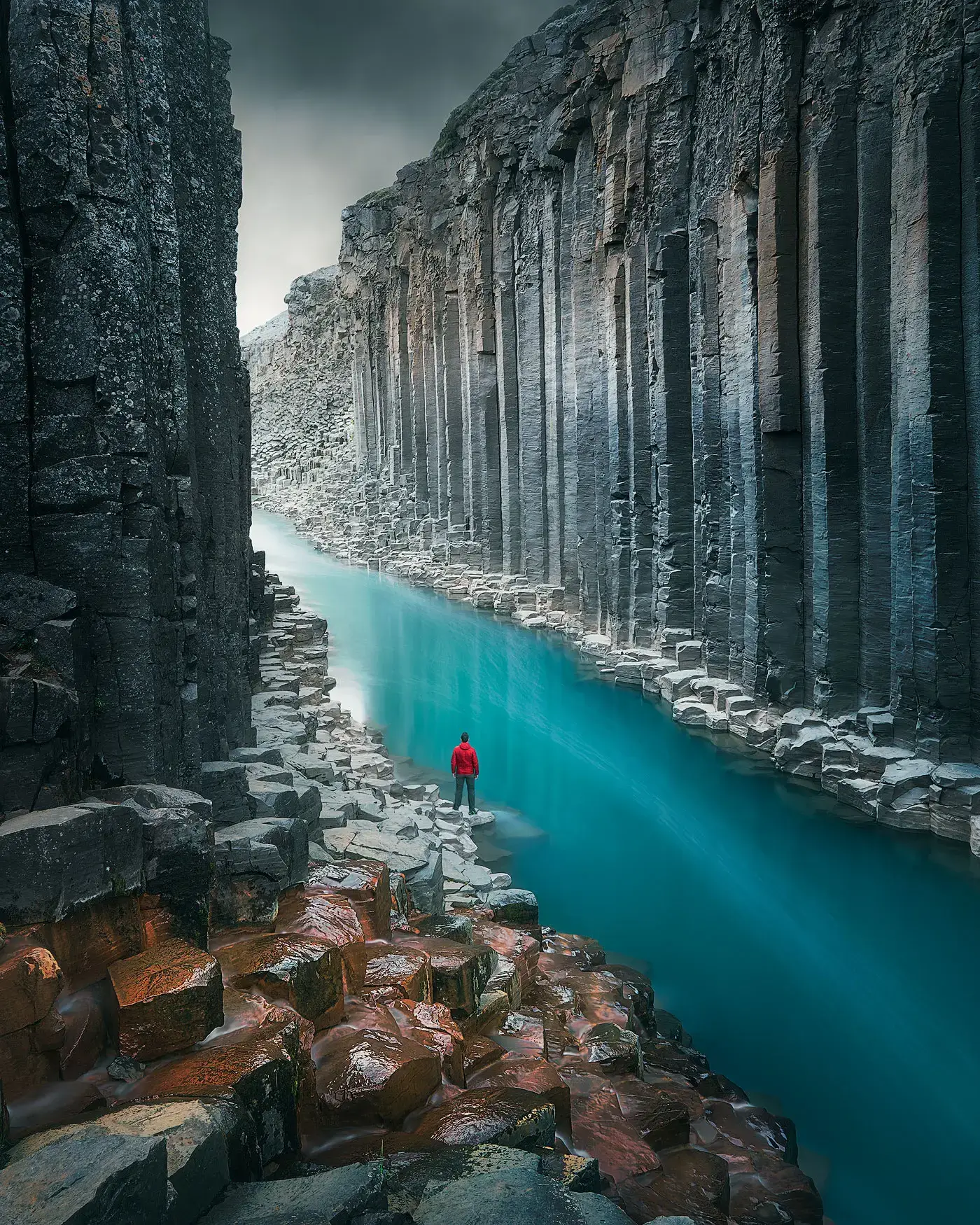 El mismo cañón con las rocas del primer plano atenuadas, de modo que la mirada va al río turquesa y a la figura de rojo
