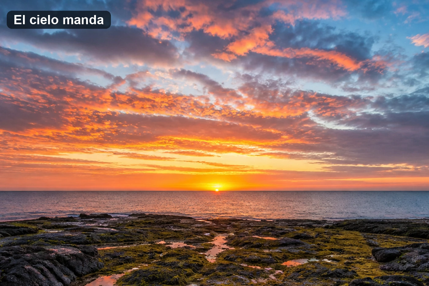 Amanecer sobre una costa rocosa con el horizonte en el tercio inferior y el cielo de nubes anaranjadas ocupando dos tercios del encuadre