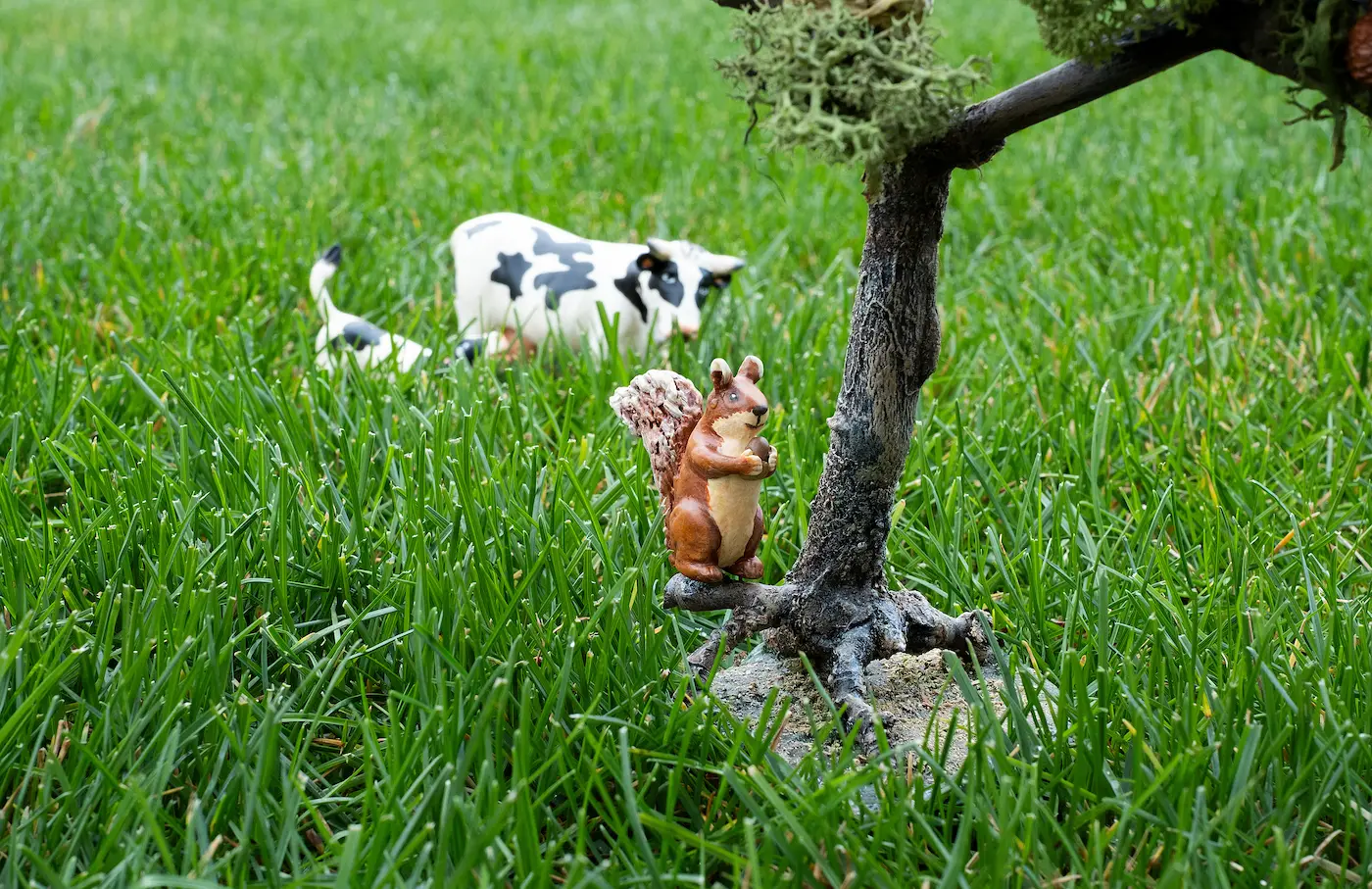 Figura de una ardilla sobre la hierba fotografiada con una apertura cerrada: tanto la figura como la vaca del fondo salen nítidas