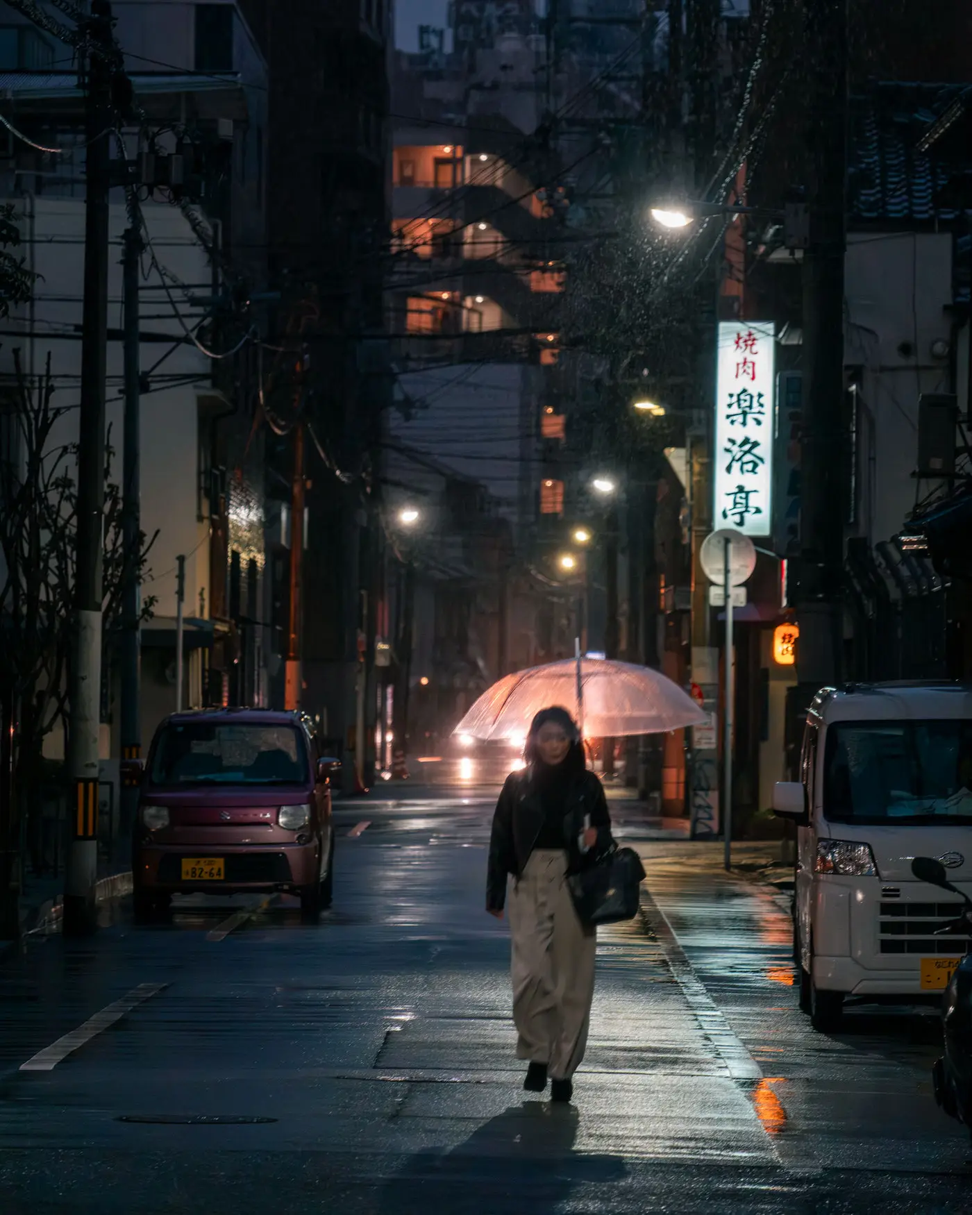 Calle japonesa de noche fotografiada a 1/15 de segundo: la persona que camina con el paraguas sale movida