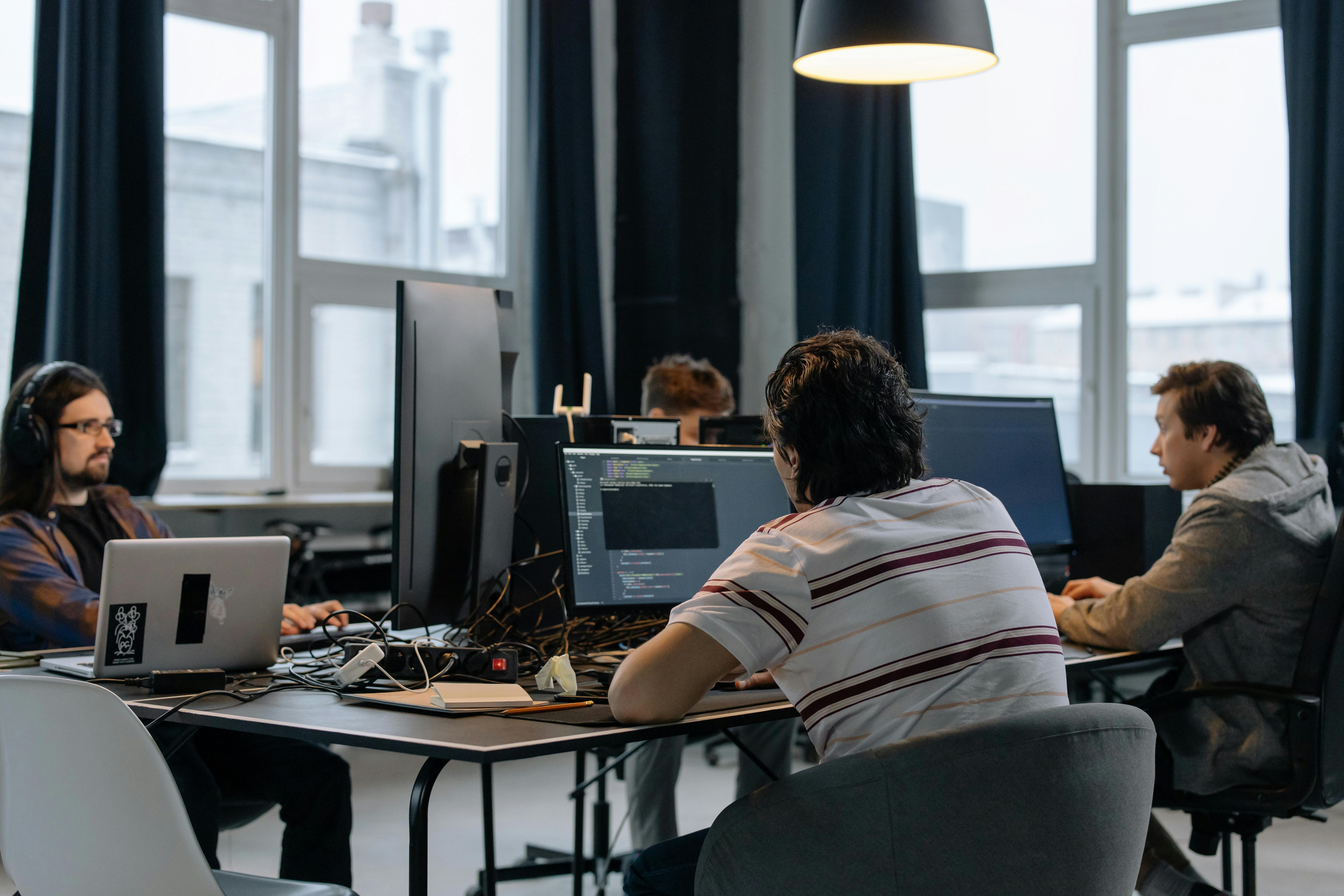 Group of young professionals working on computers in a modern office with large windows.