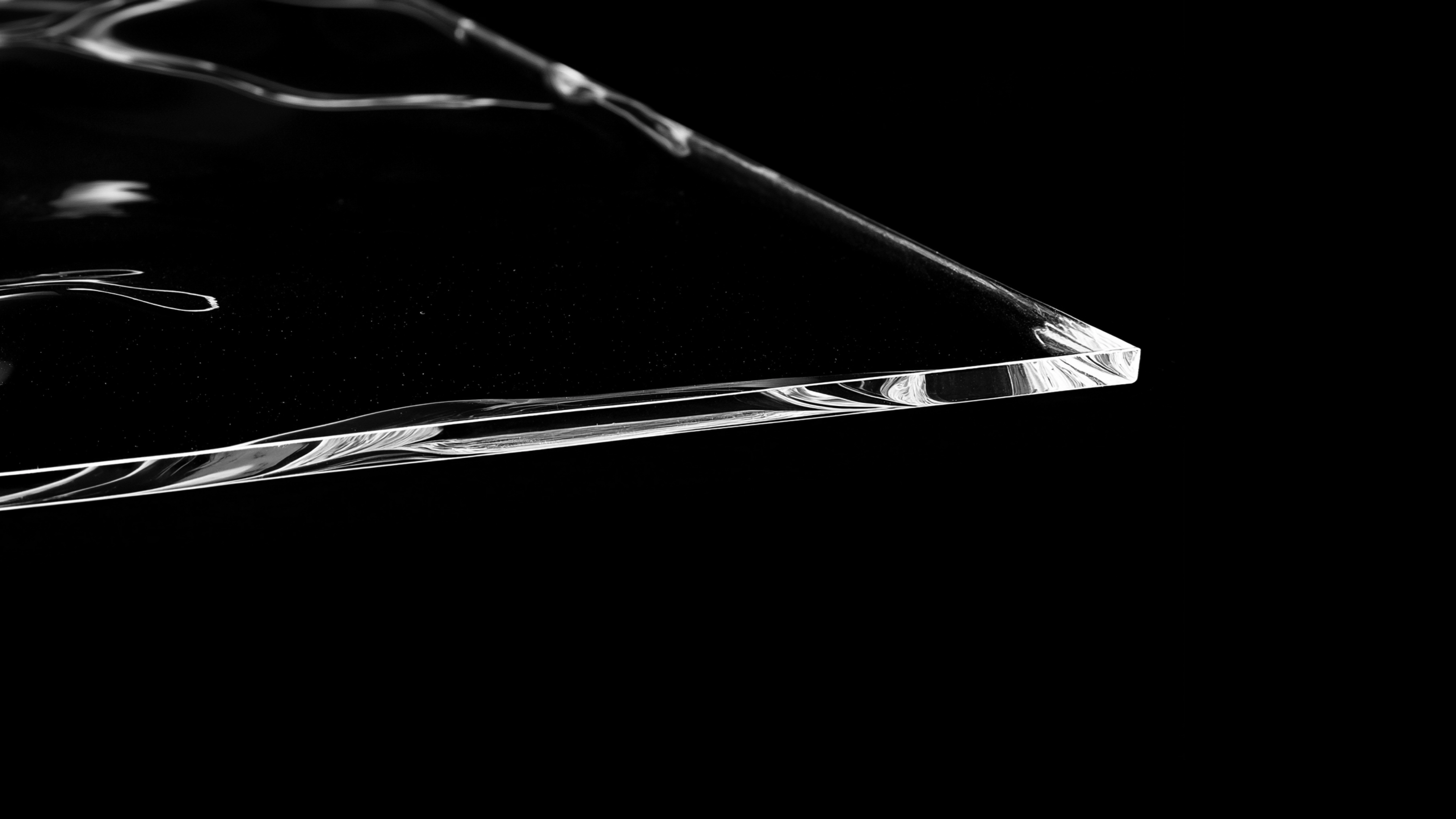 Nahaufnahme einer glatten, transparenten Glasfläche mit klaren Kanten auf schwarzem Hintergrund.