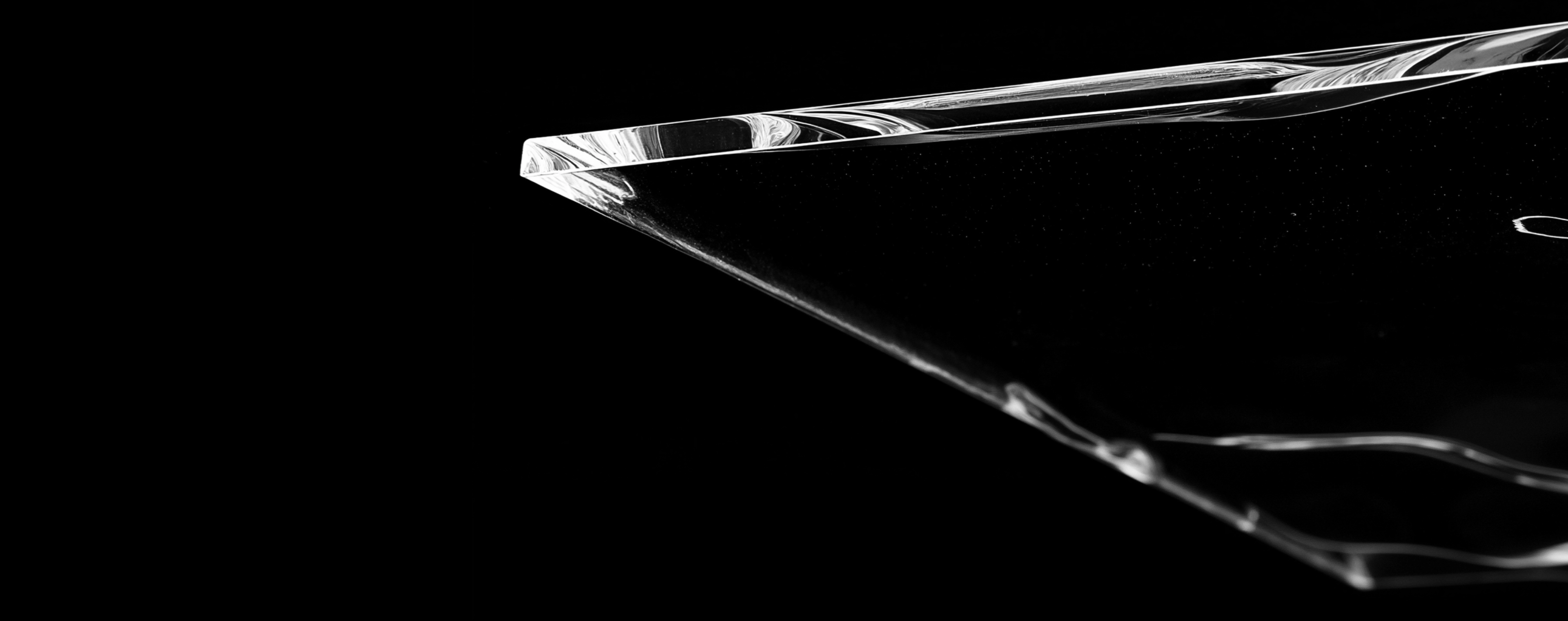 Nahaufnahme der scharfen Kante eines transparenten, gläsernen Objekts vor schwarzem Hintergrund.