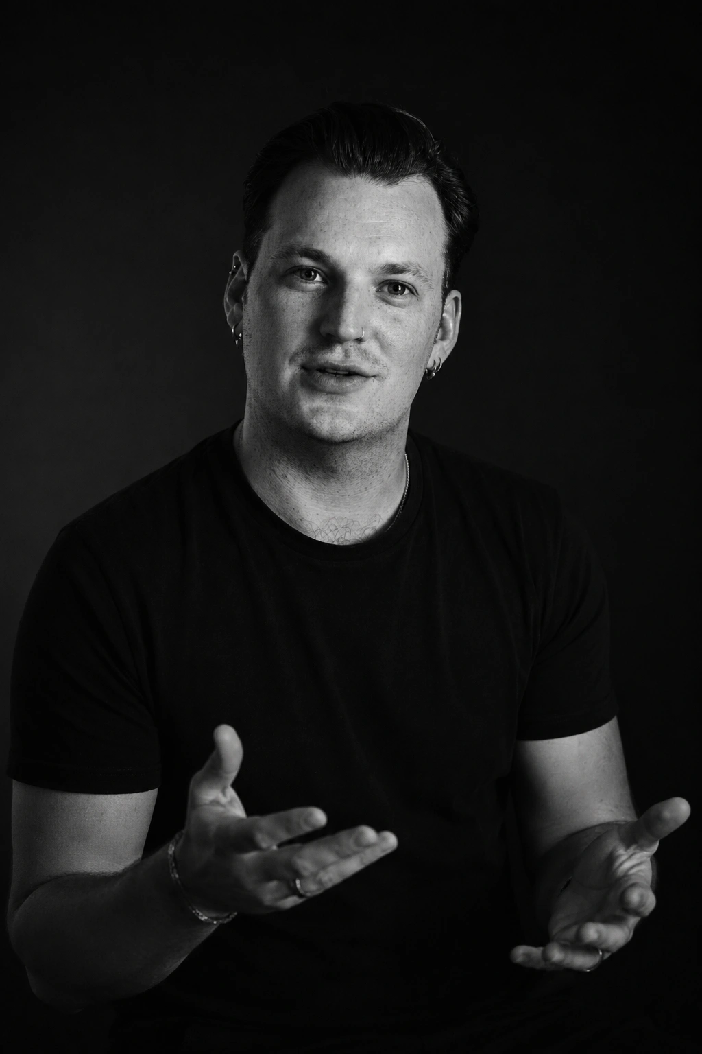Mathias Schindler in schwarzem T-Shirt spricht mit offenen Händen vor schwarzem Hintergrund.