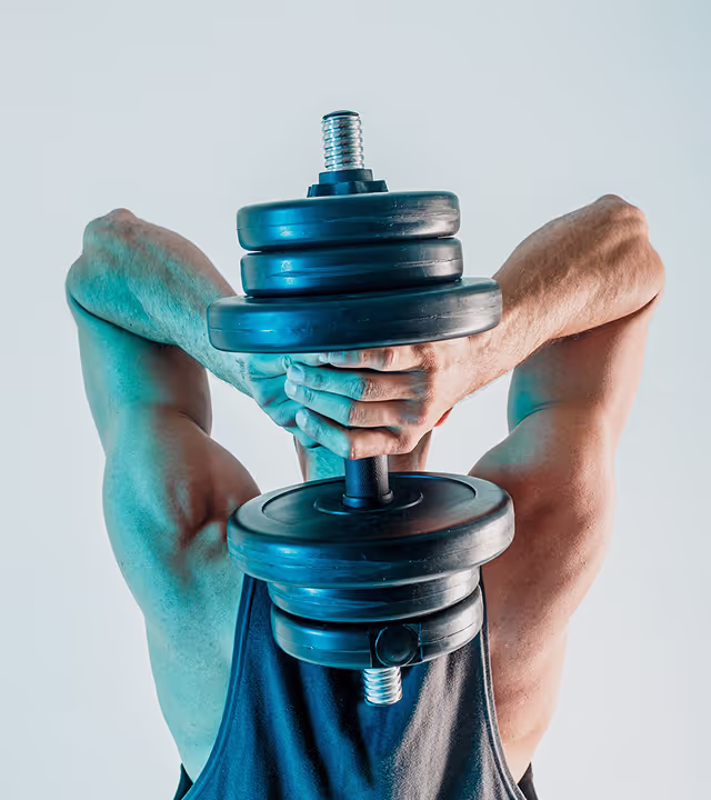 Muscular man holding a black dumbbell behind his head, performing an overhead tricep exercise.