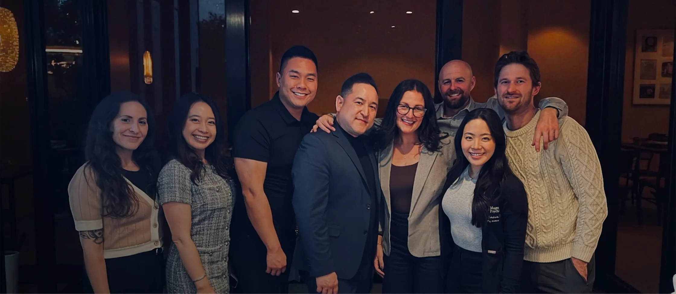 Group of eight diverse adults smiling together indoors by a doorway.