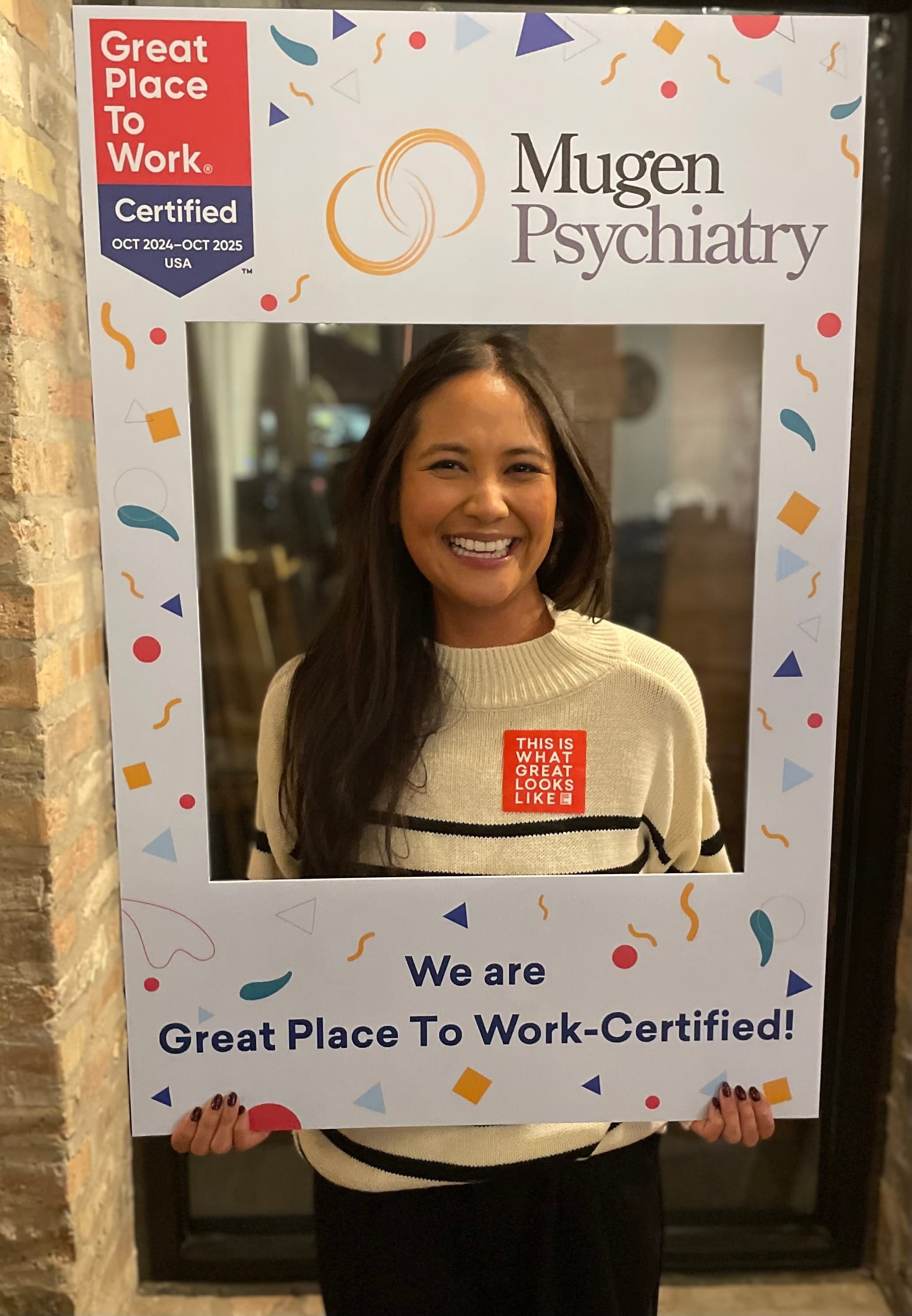 Smiling woman holding a Great Place To Work certified photo frame from Mugen Psychiatry.