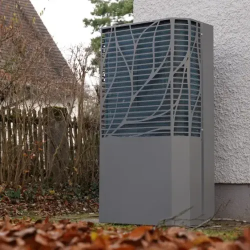 Außenstehende moderne Wärmepumpe neben einem Haus an einem herbstlichen Tag mit braunen Blättern auf dem Boden.