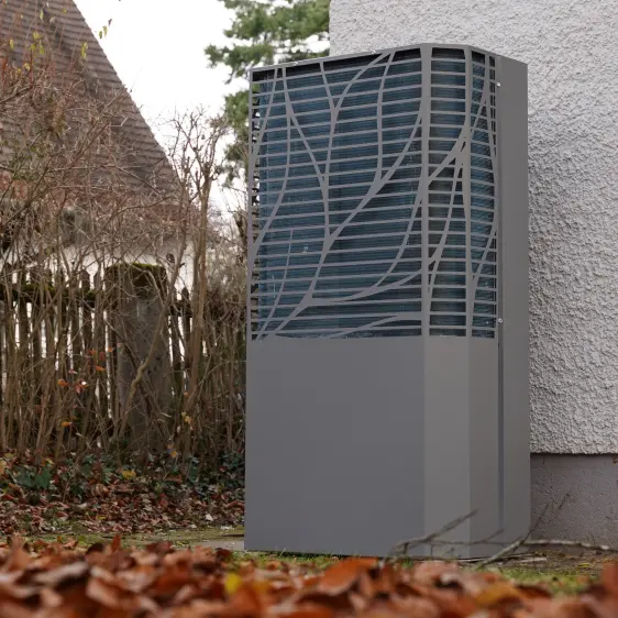 Außenstehende moderne Wärmepumpe neben einem Haus an einem herbstlichen Tag mit braunen Blättern auf dem Boden.