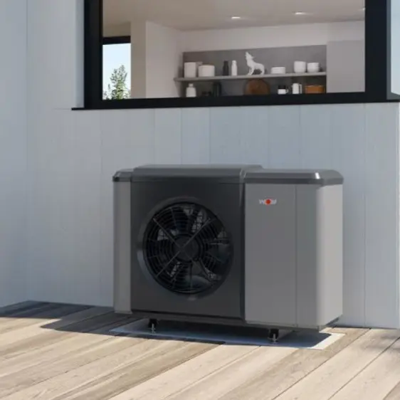 Außeneinheit einer Wärmepumpe auf einer Holzterrasse vor einem Haus mit weißer Verkleidung.