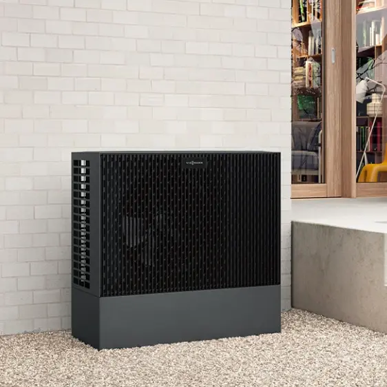 Schwarze Viessmann Wärmepumpe neben einem weißen Ziegelmauerwerk vor einem Gebäude mit großen Fenstern.