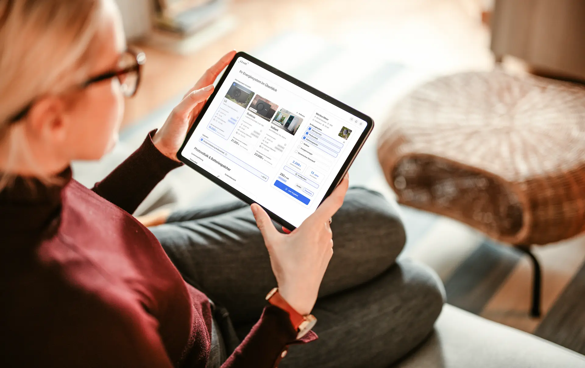 Frau sitzt auf einem Sofa und betrachtet auf einem Tablet eine Übersicht von Energiesystemen mit Preisen und Spezifikationen.