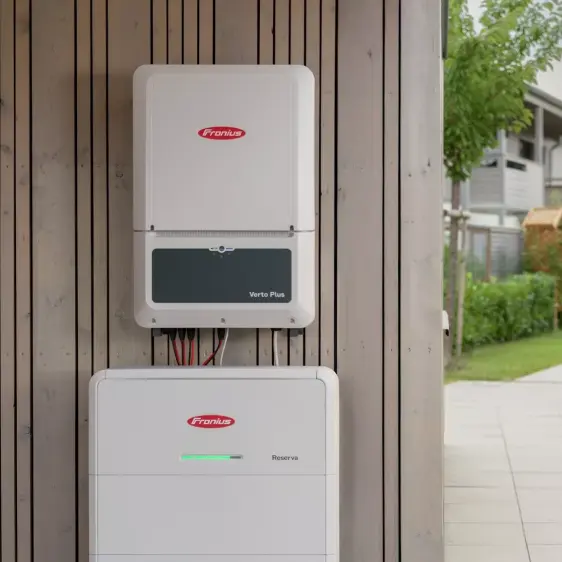 Wandmontierte Fronius Verto Plus und Reserva Geräte zur Energieverwaltung an einer Holzverkleidung im Außenbereich.