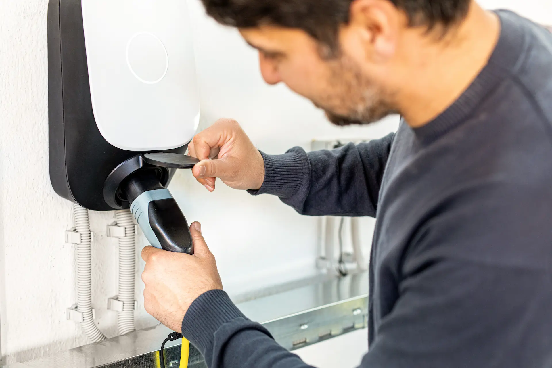 Ein Mann steckt einen Ladestecker in eine an der Wand montierte Elektroauto-Ladestation.