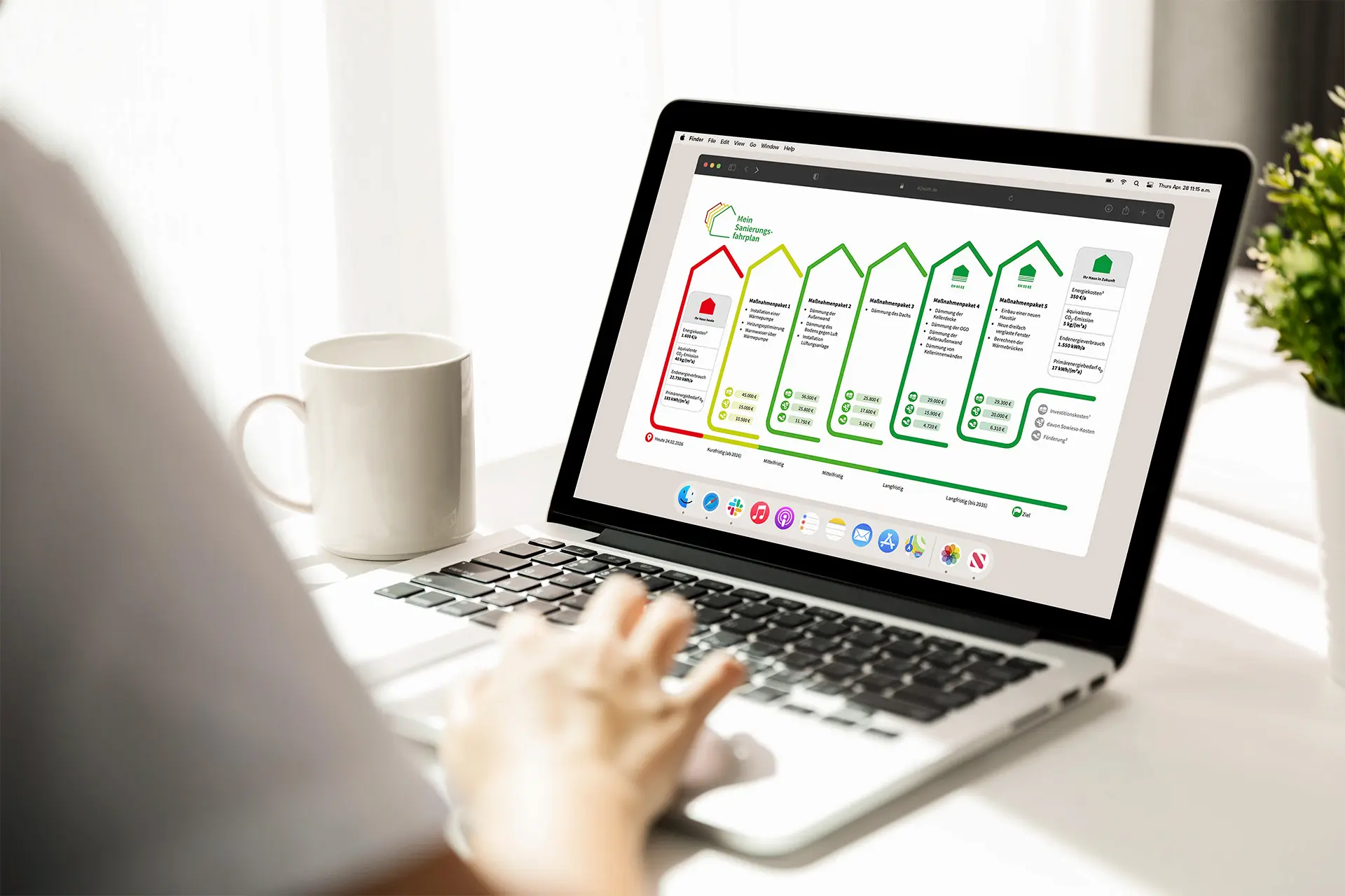 Eine Person nutzt einen Laptop, auf dessen Bildschirm eine Webseite mit einem Sanierungsfahrplan in Form von farbigen Haus-Symbolen und Kostenangaben angezeigt wird.