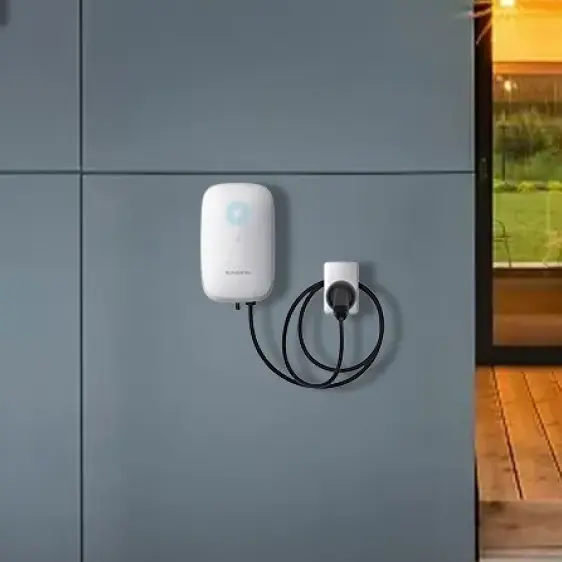Weiße Wandladestation mit schwarzem Kabel an einer blauen Wand neben einem hell erleuchteten Fenster.