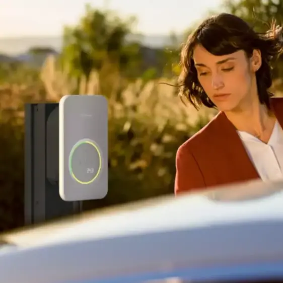 Frau steht neben einem Elektroauto, das an einer modernen Ladestation im Freien geladen wird.