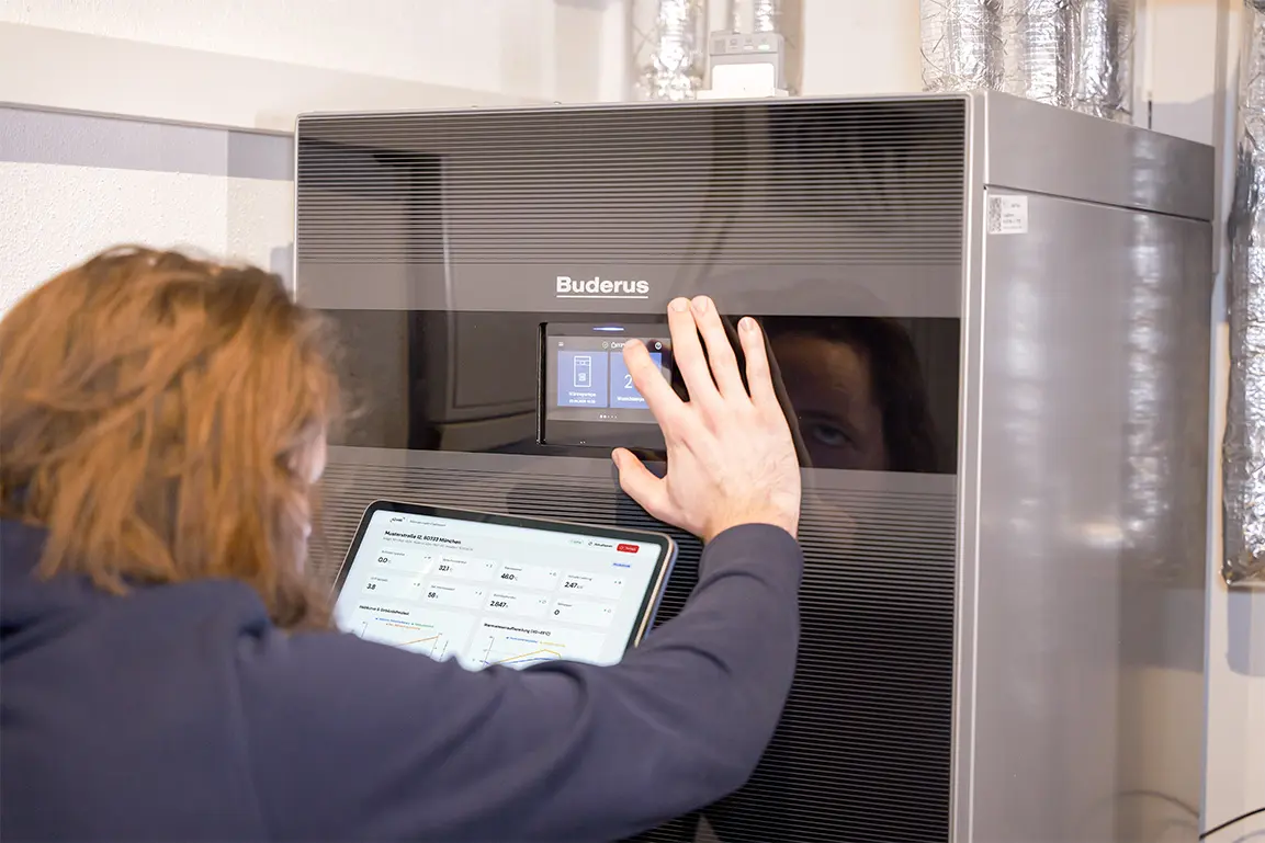 Person, der ein digitales Display eines modernen Buderus Heizsystems bedient und gleichzeitig ein Tablet mit Daten zur Energieüberwachung hält.