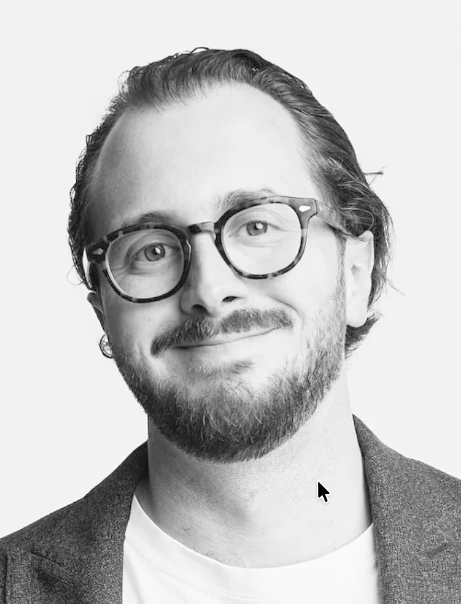 Porträt eines lächelnden Mannes mit kurzen braunen Haaren und blauem Hemd vor hellem Hintergrund.