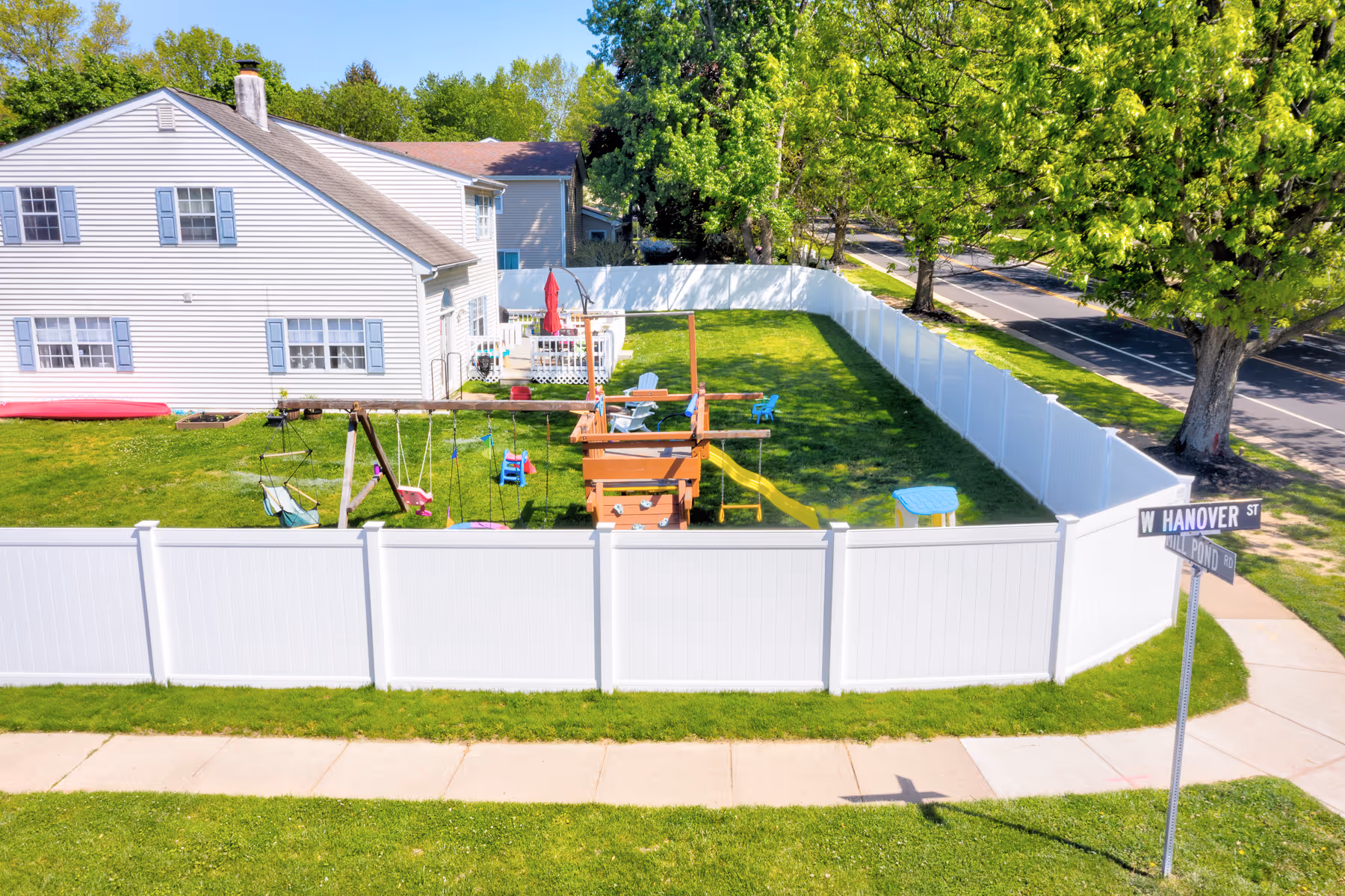 White vinyl fence enclosing a backyard with a playset, swings, slide, and green lawn.