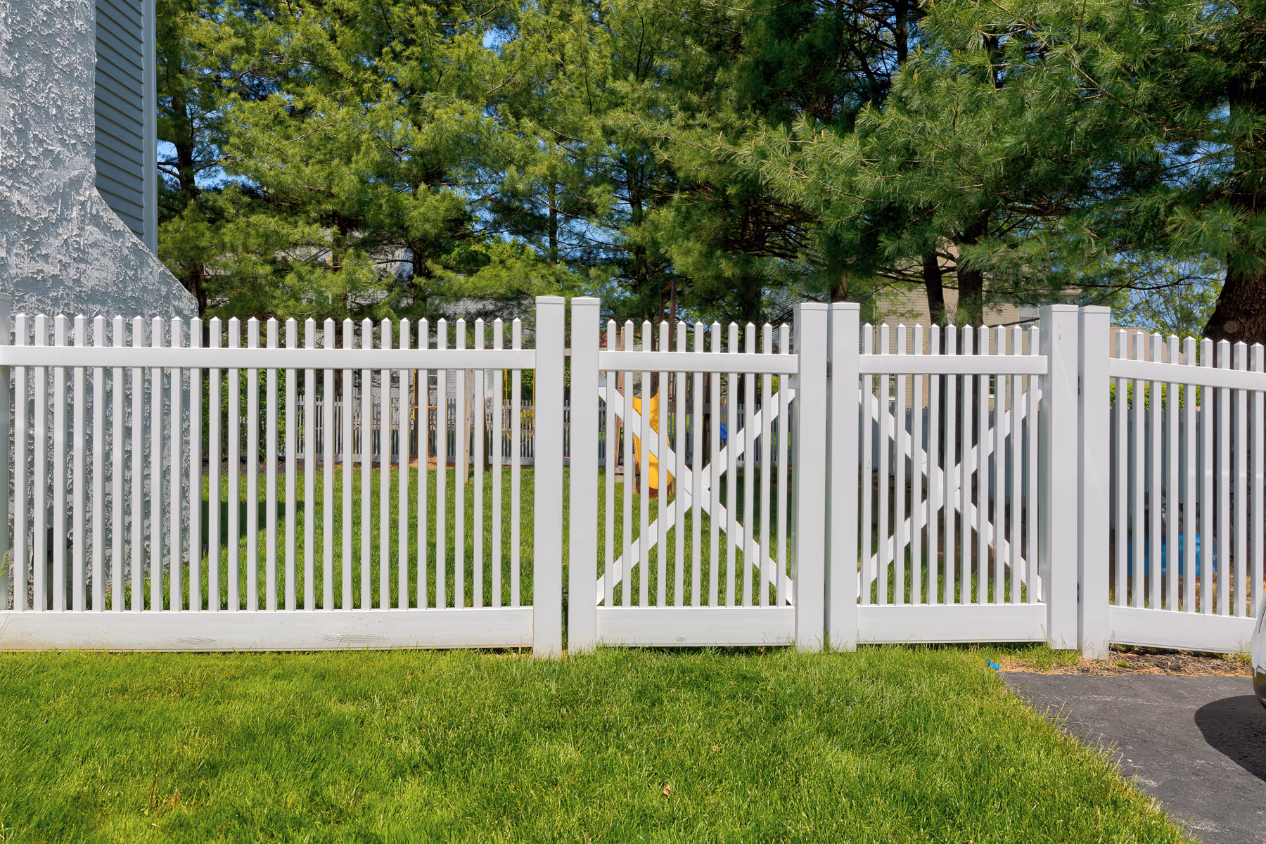 White vinyl fence with vertical slats and two gate sections enclosing a green yard with trees.