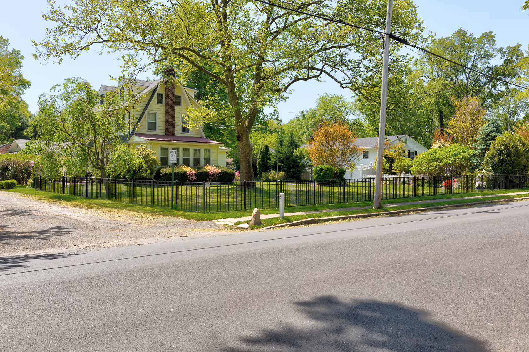 Black aluminum fence surrounding a large yard with trees and two houses on a sunny day.