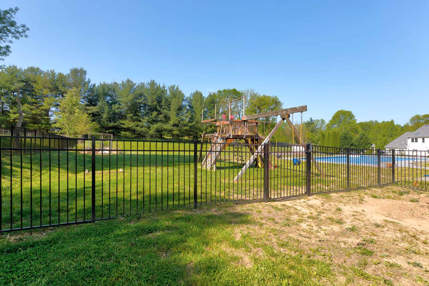 Black metal fence enclosing a backyard with a wooden playset and swings on green grass.