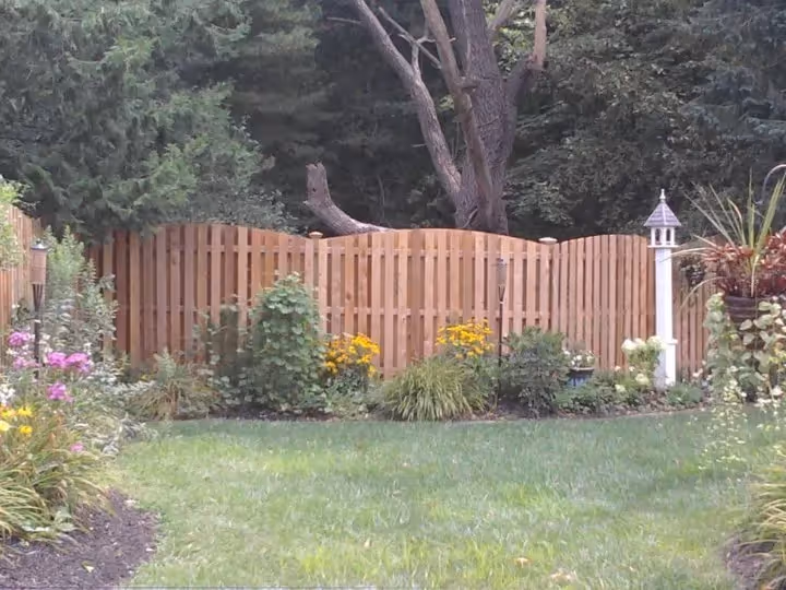 Wooden fence with curved top panels enclosing a garden with colorful flowers and green grass.