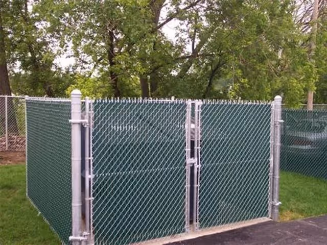 Green chain-link fence enclosure with silver metal posts and a double gate in a backyard.