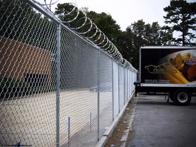 Chain-link fence topped with barbed wire next to a parking lot with a Prime Meats delivery truck.